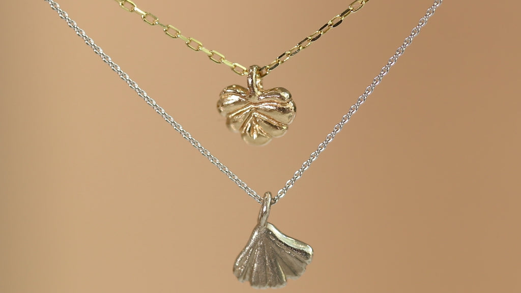 Lifestyle video showing Ginkgo Necklace in 14k white gold and Lotus Necklace in 14k yellow gold hanging together