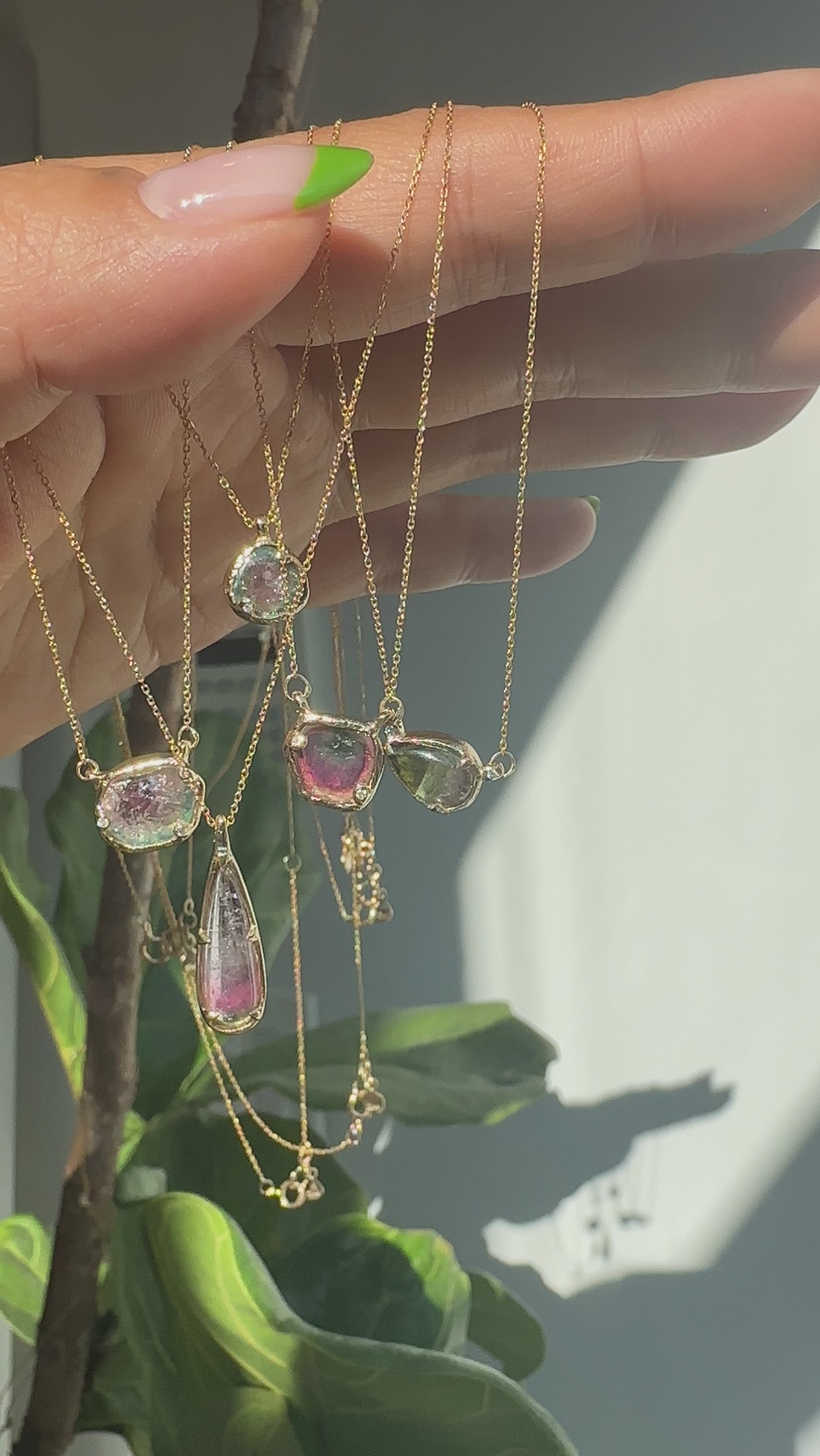 Model holds an array of pendants by Ariko featuring watermelon colored tourmalines and white diamonds